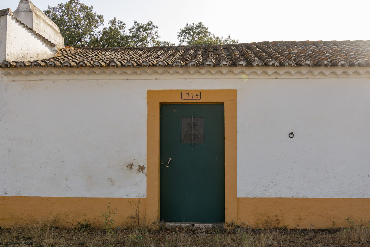 Fachada caiada de um monte alentejano, com porta verde e barra amarela